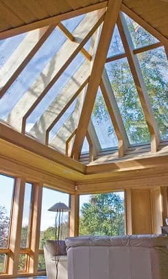 A timber-framed pyramid skylight structure daylighting a room from a vaulted ceiling.
