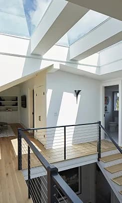 Large span skylights overhead in an open stairwell and landing, with daylight reaching the floor below.