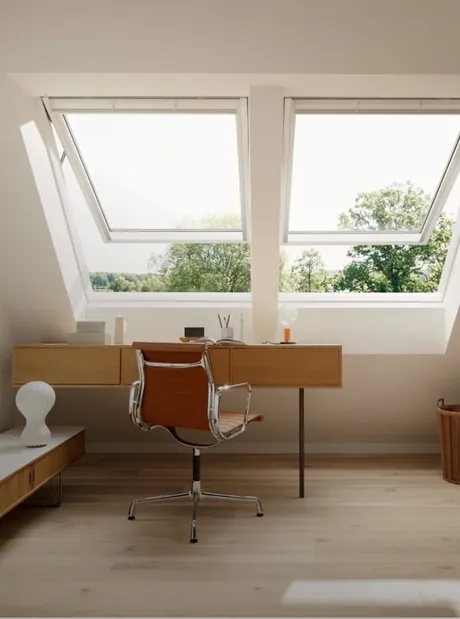 VELUX top-hinged roof window opened outward above a desk in a bright room.