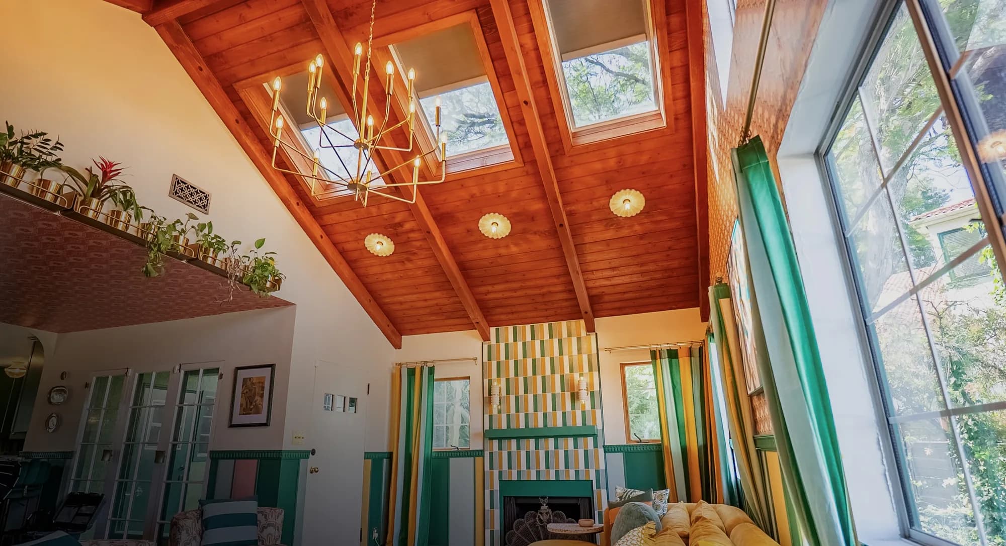 A run of VELUX skylights set into a vaulted timber ceiling, daylighting an open living space with tall windows beyond.