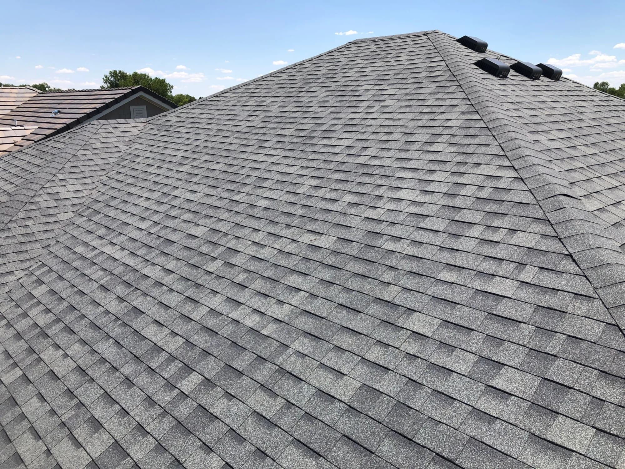 Aerial view across a completed gray asphalt shingle roof and its ridge and pipe vents in Green Valley Ranch.