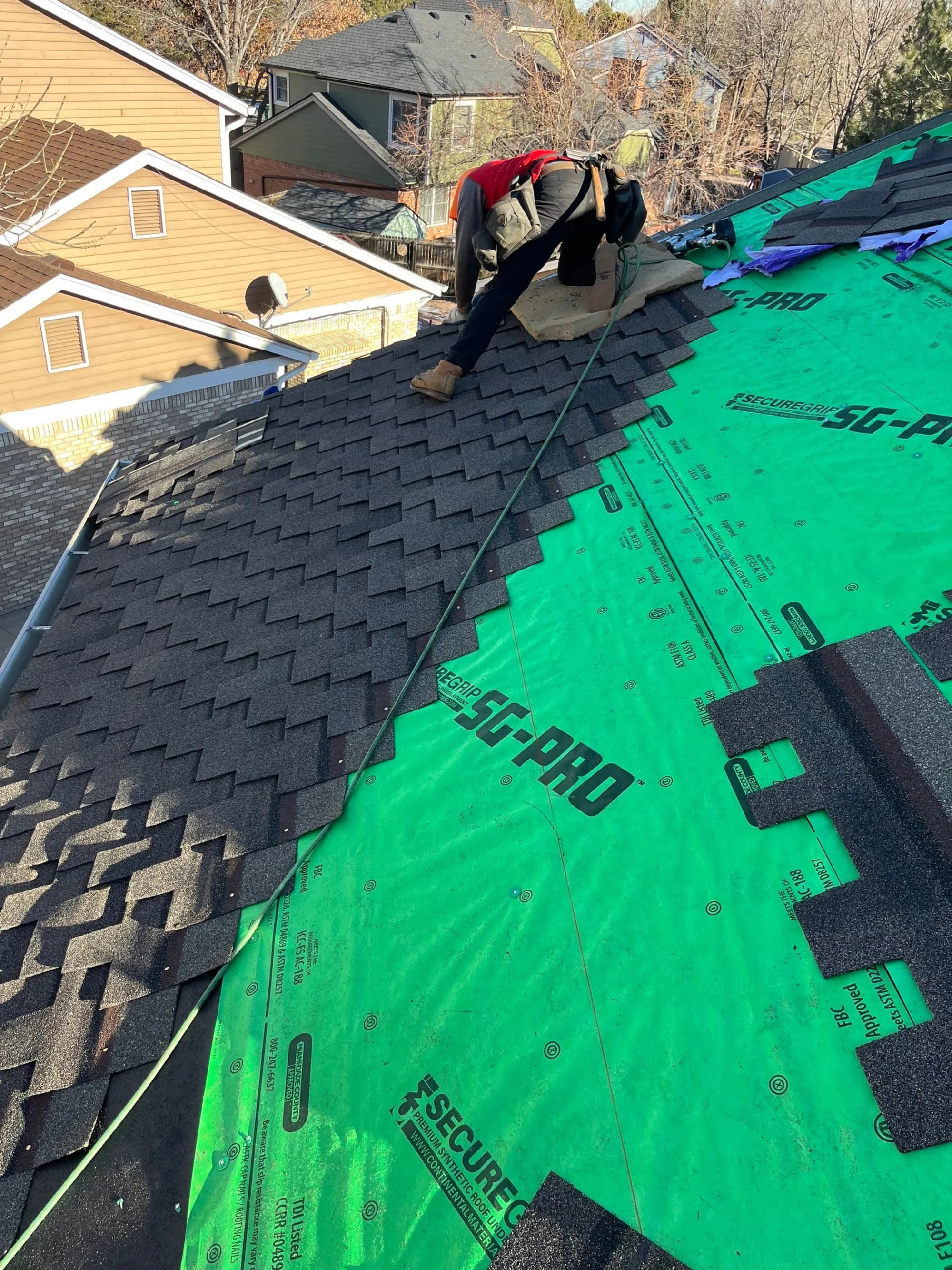Red Hawk installer laying shingles over synthetic underlayment on a Thornton roof.